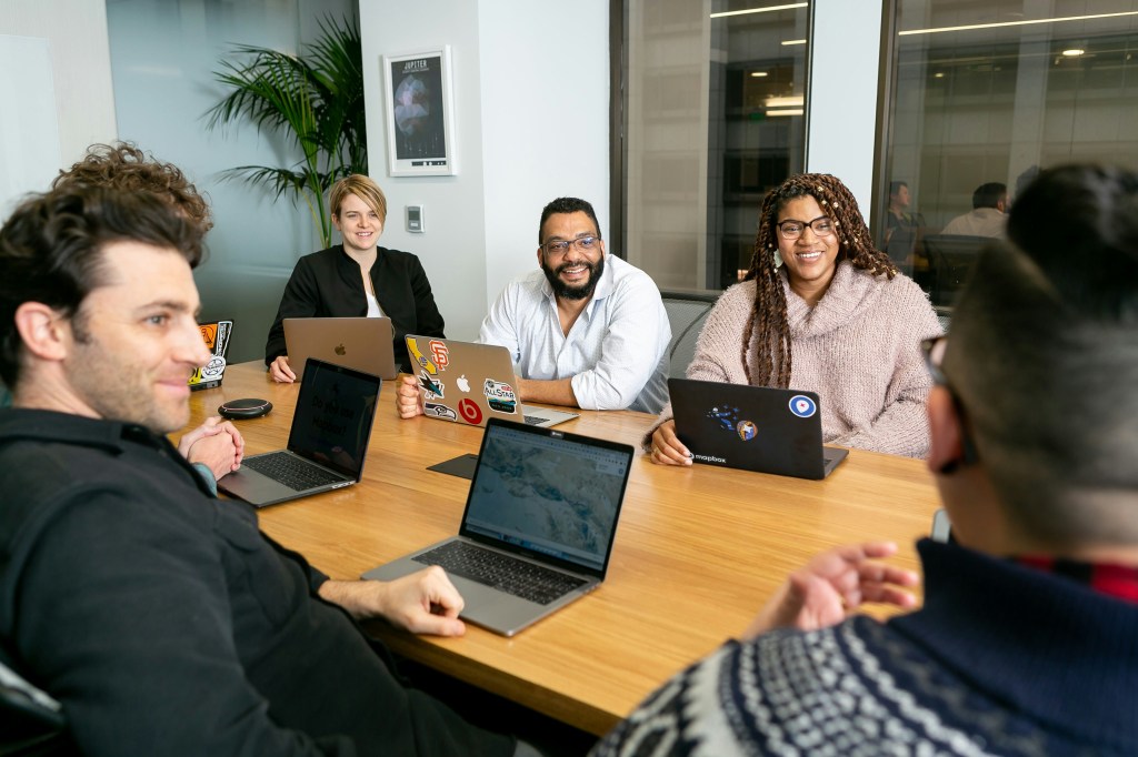 A team gathered around a table with laptops, working through ideas together