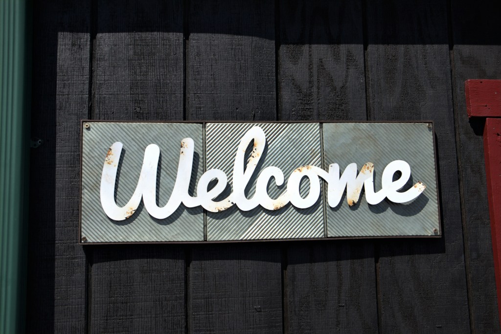 White script Welcome sign mounted on a dark wood wall