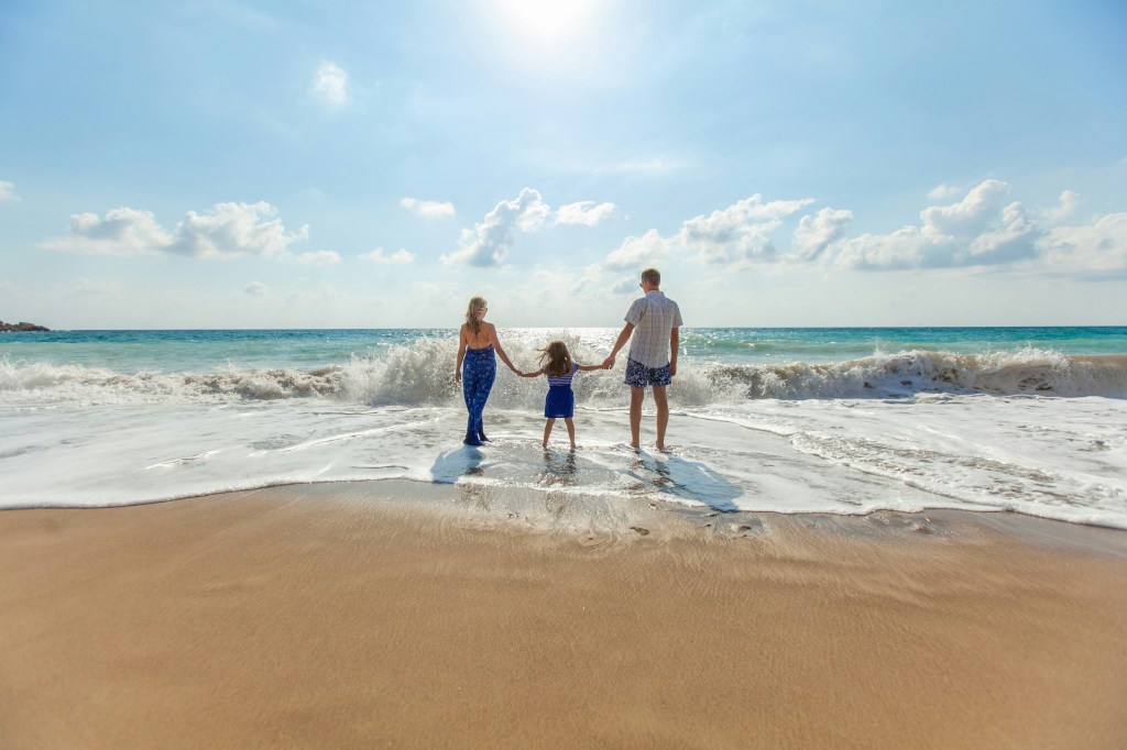 Family holding hands at the edge of the ocean, facing the waves