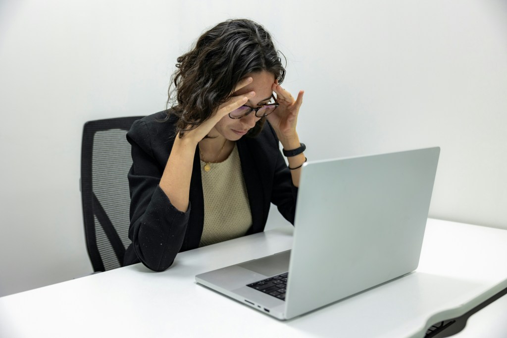 Professional at her laptop with her head in her hands, looking stressed
